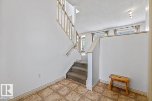 Entryway featuring square tan floor tiles, a carpeted staircase with a wood banister, and a half wall - 8509 7 Avenue, Edmonton, AB 
