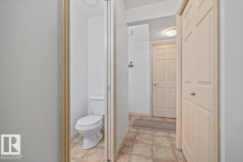 Powder room with a white toilet and neutral tile flooring - 8509 7 Avenue, Edmonton, AB 
