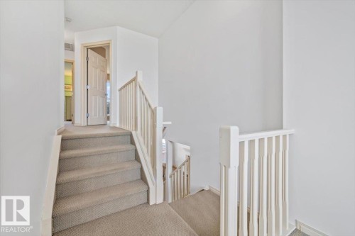 Carpeted staircase featuring white balusters and handrails, leading to a hallway with a paneled interior door - 8509 7 Avenue, Edmonton, AB 
