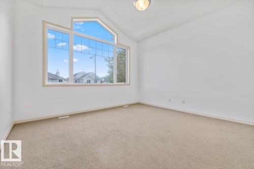 Vaulted ceiling room featuring a large geometric window, neutral wall paint, light-toned carpet, and a ceiling-mounted light fixture - 8509 7 Avenue, Edmonton, AB 