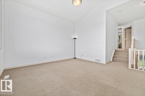 Carpeted living area featuring a vaulted ceiling and a semi-flush mount ceiling light - 8509 7 Avenue, Edmonton, AB 