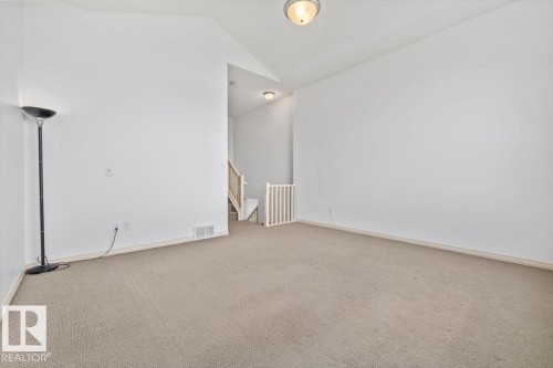 Carpeted room featuring white walls, a vaulted ceiling, and a staircase with natural wood railings - 8509 7 Avenue, Edmonton, AB 