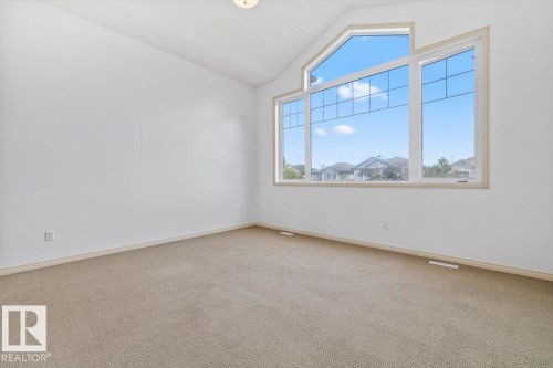 Room featuring a large window array with an arched transom, light beige carpeting, white walls, and white trim - 8509 7 Avenue, Edmonton, AB 