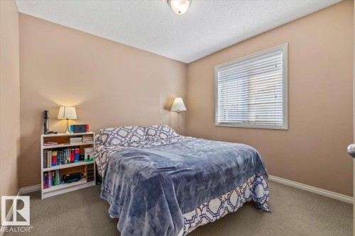 Bedroom featuring neutral wall paint, gray carpet flooring, a window with blinds, white trim, and a ceiling-mounted light fixture - 8509 7 Avenue, Edmonton, AB 