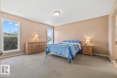 Carpeted room featuring two windows, an arched entryway, and a flush-mount ceiling light fixture - 8509 7 Avenue, Edmonton, AB 