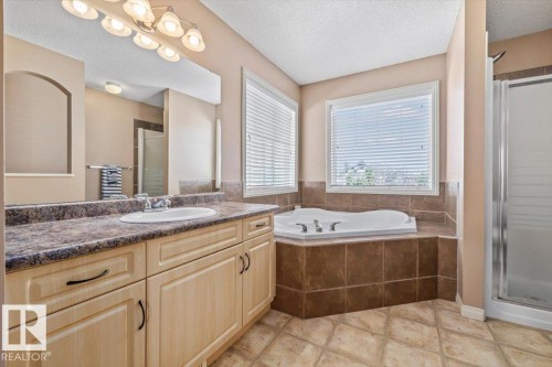 Bathroom featuring a corner soaking tub, a stand-up shower, and a vanity with an integrated sink - 8509 7 Avenue, Edmonton, AB 