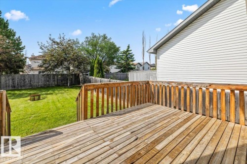 Spacious wood deck with a full railing system overlooking a fenced yard featuring mature trees and a manicured lawn - 8509 7 Avenue, Edmonton, AB 