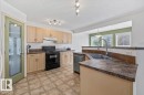 Kitchen featuring light wood-finish cabinetry, a double basin stainless steel sink, and a black appliance package including a range and dishwasher - 8509 7 Avenue, Edmonton, AB 