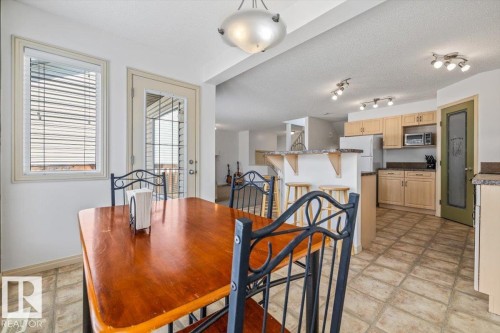 Open-concept kitchen and dining area featuring light wood cabinetry, a breakfast bar, and tile flooring - 8509 7 Avenue, Edmonton, AB 