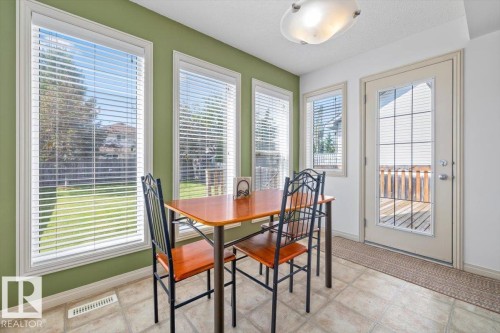 Bright dining area featuring multiple large windows, a glass-paneled exterior door, neutral-toned tiled flooring, and a semi-flush mount ceiling light fixture - 8509 7 Avenue, Edmonton, AB 