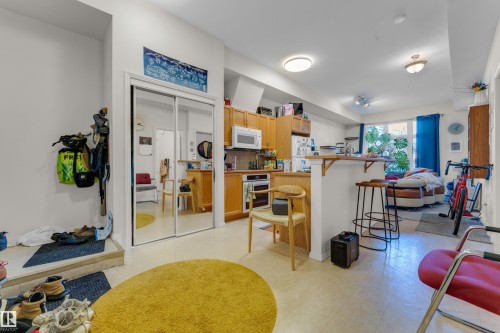 Open-concept living space featuring wood cabinetry, a built-in kitchen island with a breakfast bar, stainless steel appliances, and mirrored closet doors - 129 10407 122 Street, Edmonton, AB 