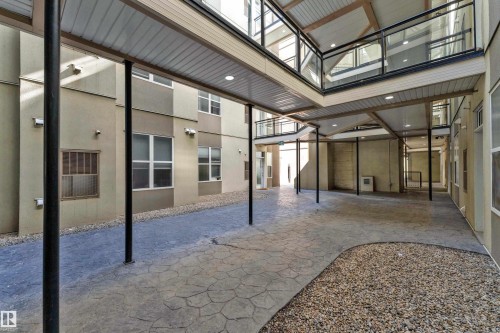 Covered courtyard area featuring stamped concrete flooring, gravel accents, and multi-level walkways with glass panel railings - 129 10407 122 Street, Edmonton, AB 