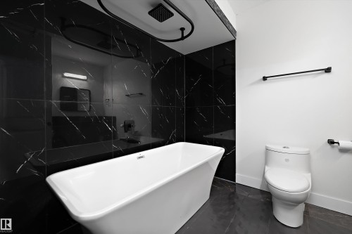 Modern bathroom in basement suite featuring a freestanding soaker tub against a wall of black marble-look tile - 6084 179 Avenue, Edmonton, AB 