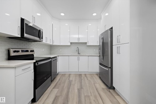 Modern kitchen featuring white cabinetry, stainless steel appliances, light wood-finish flooring, recessed lighting, and a subway tile backsplash - 6084 179 Avenue, Edmonton, AB 