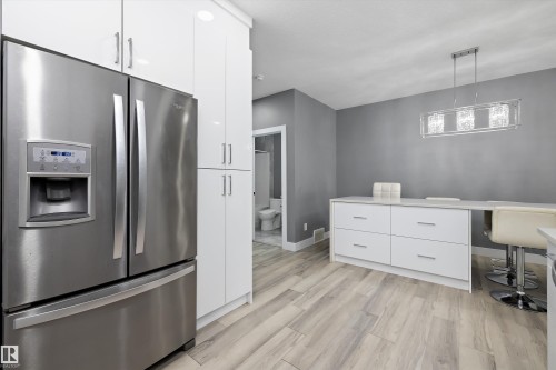 Modern kitchen featuring wood-finish flooring, stainless steel French door refrigerator, and white cabinetry - 6084 179 Avenue, Edmonton, AB 