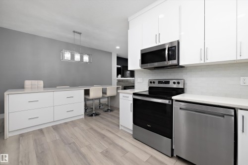 Modern kitchen featuring white cabinetry, stainless steel appliances, a white subway tile backsplash, and light wood-finish flooring - 6084 179 Avenue, Edmonton, AB 