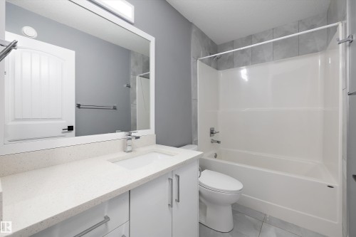 Modern bathroom featuring a white vanity with an integrated sink, a light-toned countertop, and chrome fixtures - 6084 179 Avenue, Edmonton, AB 