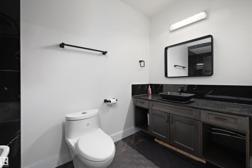 Modern bathroom featuring a dark wood-finish vanity with a vessel sink, black countertop, and black-framed mirror - 6084 179 Avenue, Edmonton, AB 