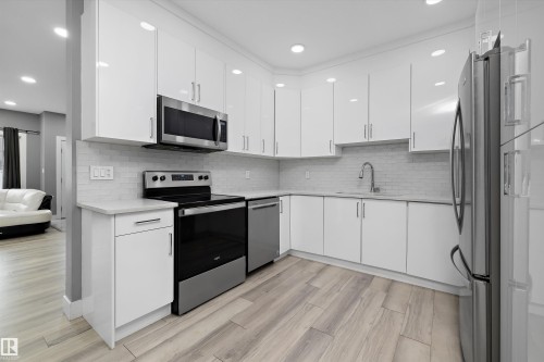 Modern kitchen featuring white cabinetry, stainless steel appliances, light-toned countertops, and a subway tile backsplash - 6084 179 Avenue, Edmonton, AB 