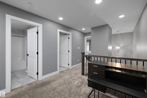 Carpeted hallway featuring recessed lighting, a built-in dark wood-finish desk, and a modern geometric light fixture - 6084 179 Avenue, Edmonton, AB 
