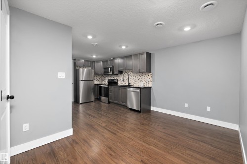 Modern kitchen featuring stainless steel appliances, dark wood-finish cabinetry, black countertops, and a patterned tile backsplash - 6084 179 Avenue, Edmonton, AB 