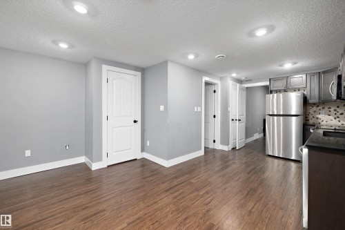 Open-concept area featuring wood-finish flooring, recessed lighting, and a kitchen area with stainless steel appliances, dark cabinetry, and a stone backsplash - 6084 179 Avenue, Edmonton, AB 