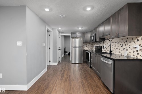 Kitchen featuring dark grey cabinetry, black countertops, stainless steel appliances, a black faucet, and a patterned tile backsplash - 6084 179 Avenue, Edmonton, AB 