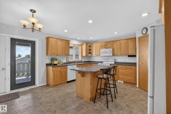 Kitchen featuring extensive wood cabinetry, a central island with countertop seating, white appliances, recessed lighting, and tile-finish flooring - 
