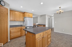 Kitchen featuring wood cabinetry, a central island with a dark countertop, recessed lighting, and tile flooring - 