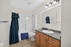 Bathroom featuring a wood-finish vanity with a dark countertop, an oval undermount sink, and a three-light vanity fixture - 