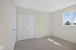 Carpeted room featuring a double bifold closet, a white framed window with clear glass, a white paneled door with a black handle, and light neutral wall paint - 