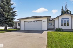 White siding exterior featuring a two-car garage with decorative window inserts, an arched accent window, a concrete driveway, a front walkway, and a manicured lawn - 