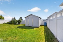 Expansive lawn area featuring a storage shed with a metal roof and a white privacy fence - 