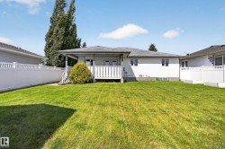 Expansive grass lawn featuring a white vinyl privacy fence, a covered deck with white railings, and mature landscaping - 