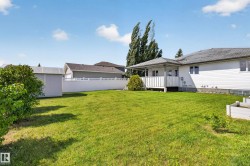 Spacious fenced backyard featuring a manicured lawn, a covered porch, white vinyl siding, and a detached storage shed - 
