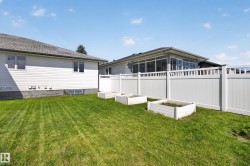 Fenced backyard featuring a manicured lawn, three raised garden beds, and a sunroom with ample windows - 