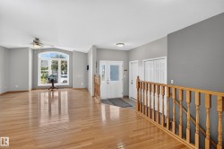 Open-concept interior featuring wood-finish flooring, vaulted ceilings, a prominent arched window, and a wood spindle railing - 
