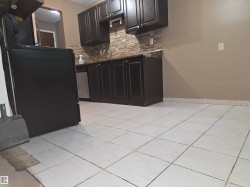 Kitchen featuring white tile flooring, dark wood-finish cabinetry, a textured backsplash, and a built-in dishwasher - 
