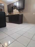 Kitchen featuring dark wood-finish cabinetry, stainless steel dishwasher, stone tile backsplash, and light-colored tile flooring - 