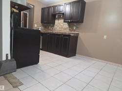 Kitchen featuring dark wood-finish cabinetry, a stone-look tile backsplash, a stainless steel sink with a gooseneck faucet, and light-toned floor tiling - 