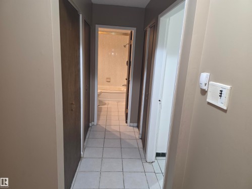 Hallway featuring neutral wall paint, white square floor tiles, and wood-panel closet doors - 307 11907 81 Street Nw, Edmonton, AB 