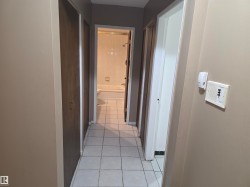 Hallway featuring neutral wall paint, white square floor tiles, and wood-panel closet doors - 