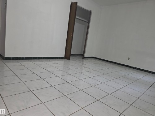 Spacious interior featuring light-toned square tile flooring with contrasting grout, white walls, and a dark baseboard trim - 307 11907 81 Street Nw, Edmonton, AB 