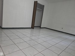 Spacious interior featuring light-toned square tile flooring with contrasting grout, white walls, and a dark baseboard trim - 