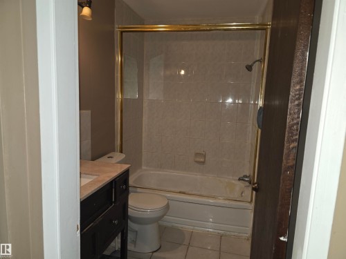 Bathroom featuring a built-in tub with tile surround, a glass shower enclosure with a gold-tone frame, and a dark wood-finish vanity with a light-toned countertop - 307 11907 81 Street Nw, Edmonton, AB 