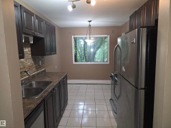Kitchen featuring dark wood-finish cabinetry, a double basin stainless steel sink, and a stacked stone backsplash - 