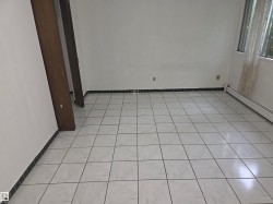 Spacious interior featuring white tile flooring, white painted walls, and dark wood-finish trim around a doorway - 