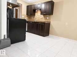 Kitchen featuring dark wood-finish cabinetry, tile backsplash, stainless steel sink, and light tile flooring - 