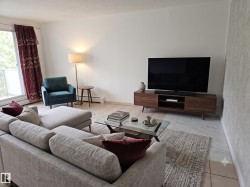 Bright living area featuring light-toned tile flooring, white wall finishes, and a large sliding glass door with a balcony - 