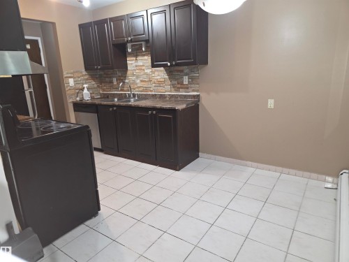 Kitchen featuring dark wood cabinetry, a stone-look tile backsplash, and white square floor tiles - 307 11907 81 Street Nw, Edmonton, AB 